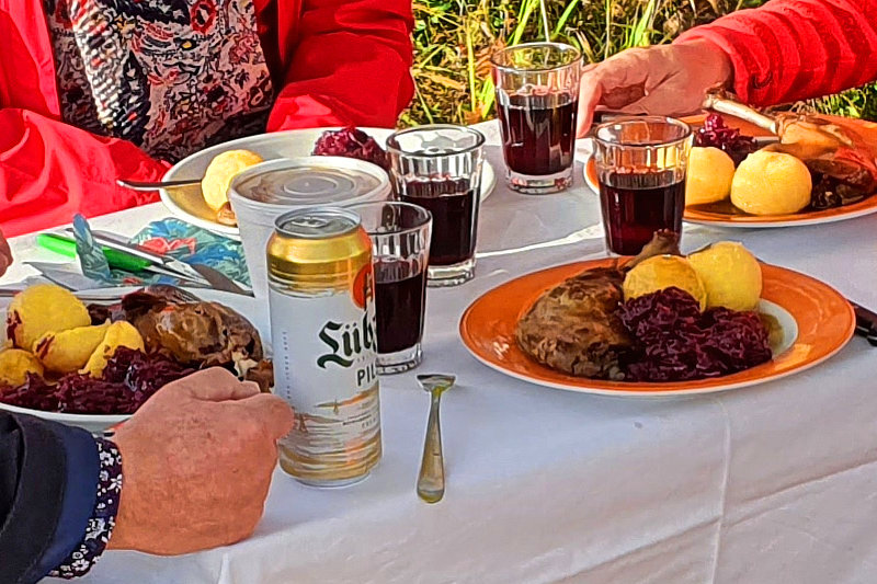 Ein Tisch mit vier Tellern auf denen ein Gänsekeule zwei Klöße und Rotkraut liegen. Außerdem vier Gläser mit Rotwein.